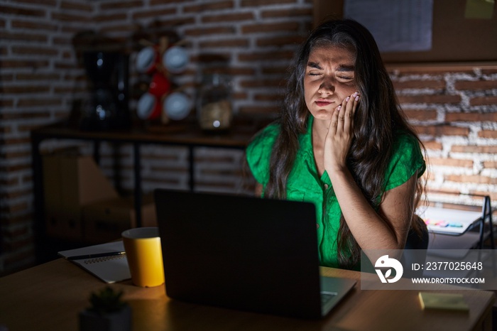 Young teenager girl working at the office at night touching mouth with hand with painful expression because of toothache or dental illness on teeth. dentist