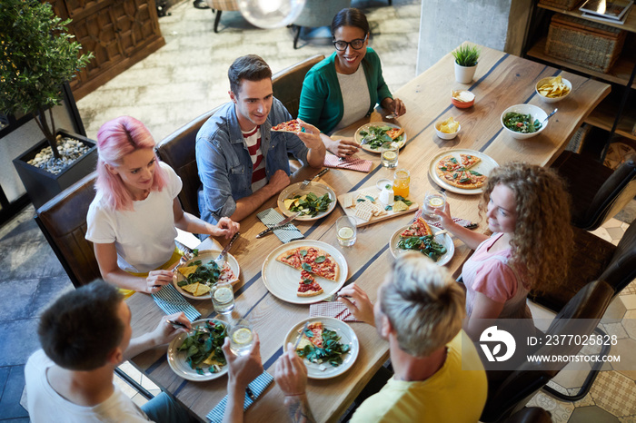 Several young friendly men and women gathered by table served with food for dinner and talk