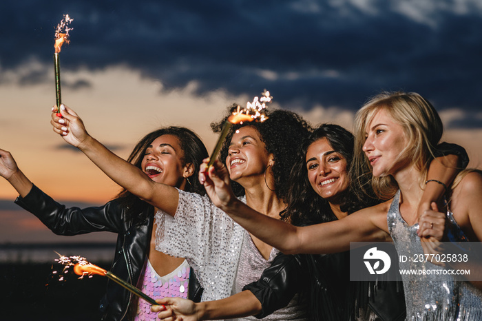 Happy friends with sparklers at sunset. Four laughing friends celebrating with fireworks outdoors.