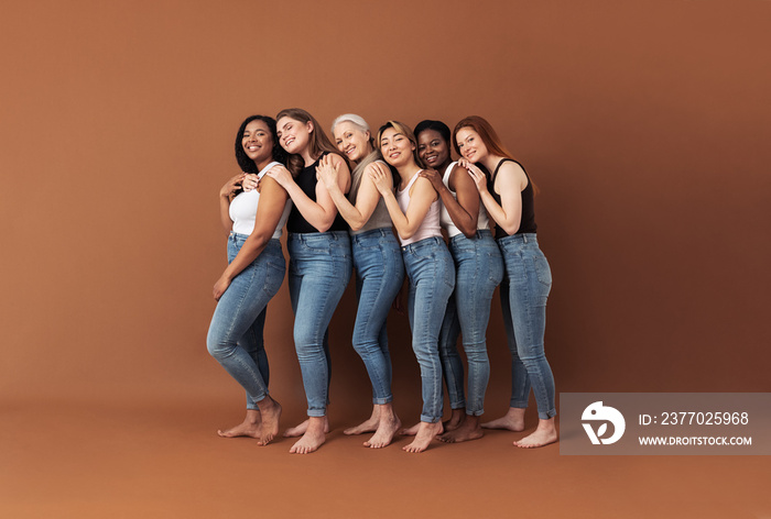 Full length of six smiling women embracing in studio. Females of different ages and body types posing over brown background.