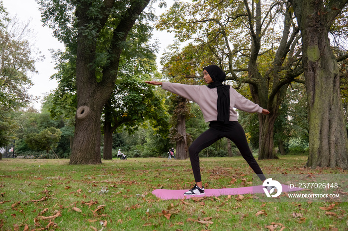 Woman in hijab in yoga warrior pose in park