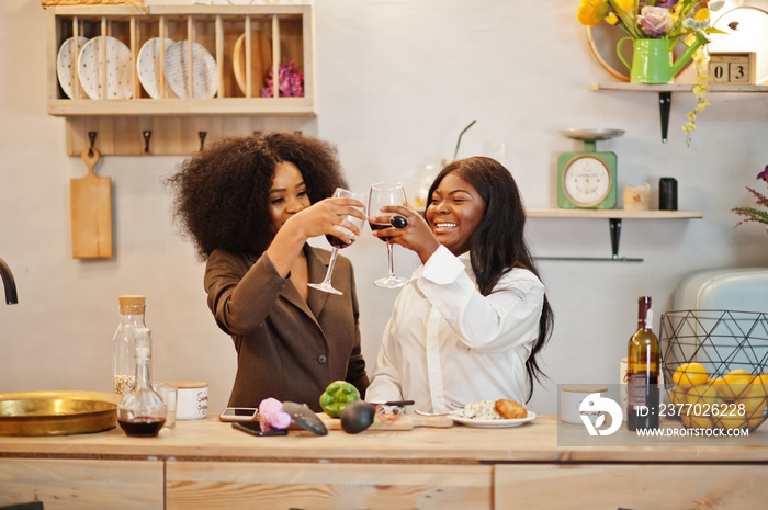 Two african american female friends women spending time at kitchen with wine. Black girlfriends  relaxing at home.