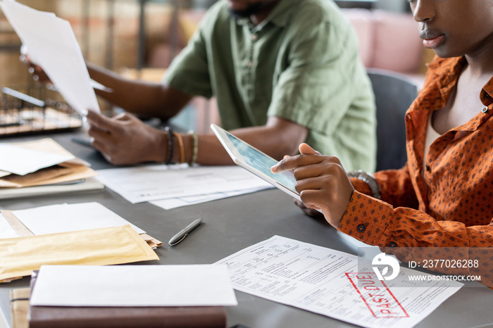 Young African female auditor pointing at tablet screen while checking online financial data and working with papers