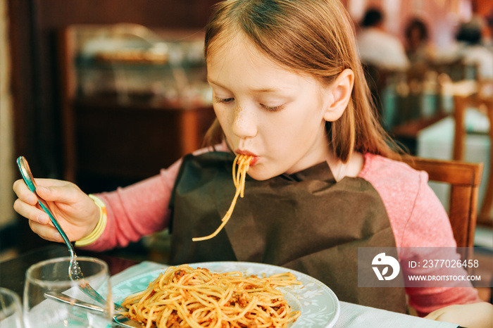 Adorable little girl eating spaghetti with bolognese sauce in the restaurant