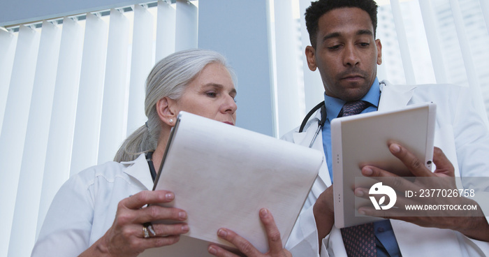 Portrait of elderly female doctor taking notes on patients results while looking at tablet computer. Two medical physicians consult over patients  health while using a portable electronic tablet