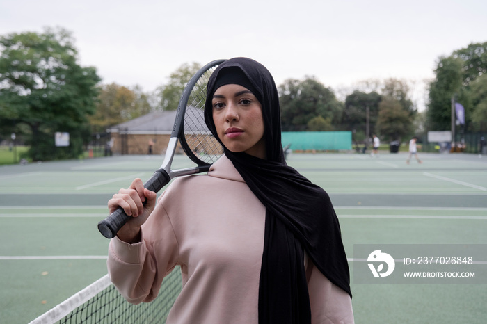 Portrait of woman in hijab holding tennis racket at tennis court