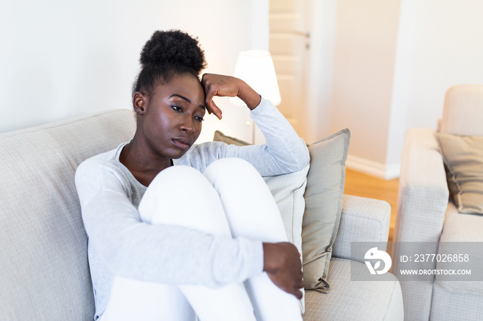 Sad thoughtful worried african american girl sit on sofa looking away feel depressed doubtful, lonely stressed upset young black girl thinking of psychological problem thinking regret about mistake