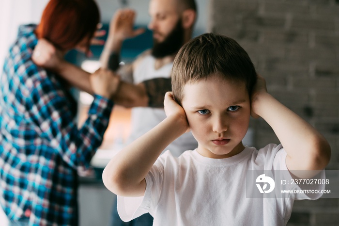 Sad child covering his ears with hands during parents quarrel.