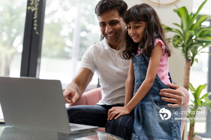 Father sitting with daughter and using laptop