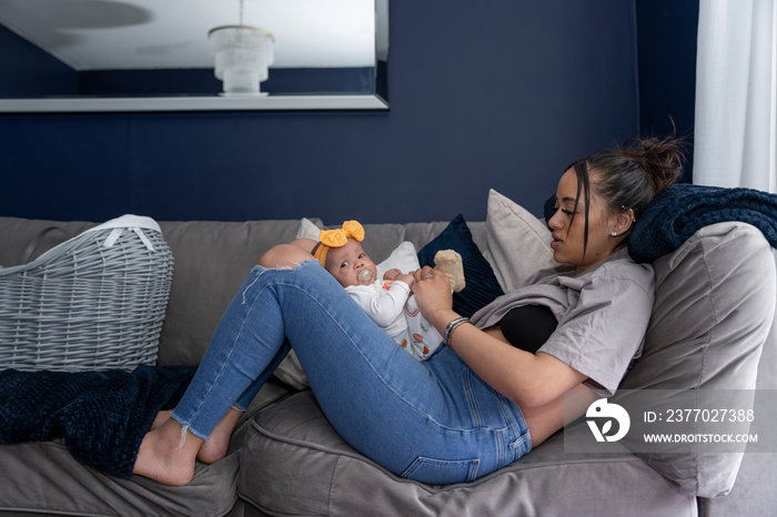 Mother relaxing with baby girl on sofa at home