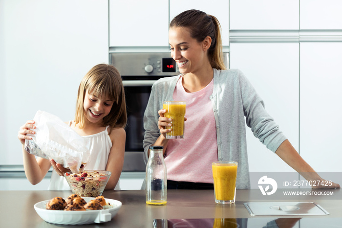 Pretty young mother and her daughter preparing breakfast in the kitchen at home.