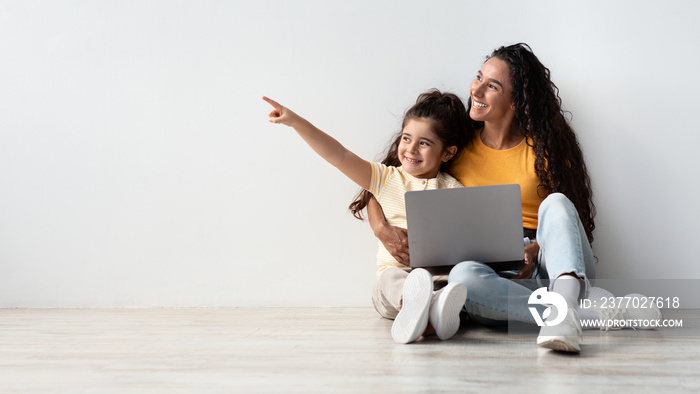 Great Offer. Happy Little Girl And Her Mom With Laptop Pointing Aside