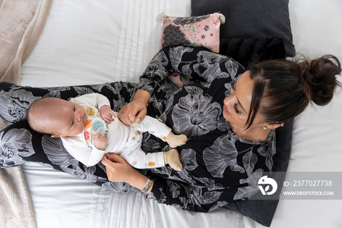 Directly above view of mother sitting with newborn baby girl on bed at home