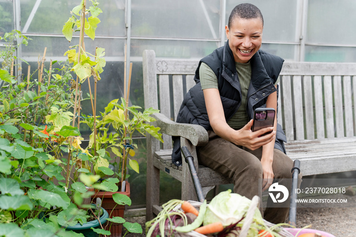 Smiling woman photographing harvested vegetables with smart phone