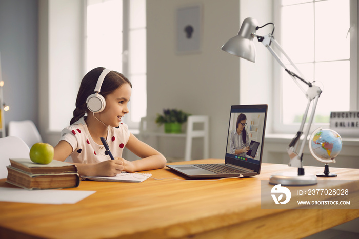 Online student education. Schoolgirl listens to a lecture of a teacher using a laptop video call lesson sitting at a table at home.