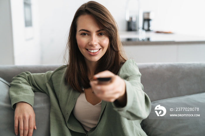 Happy young woman watching tv on sofa