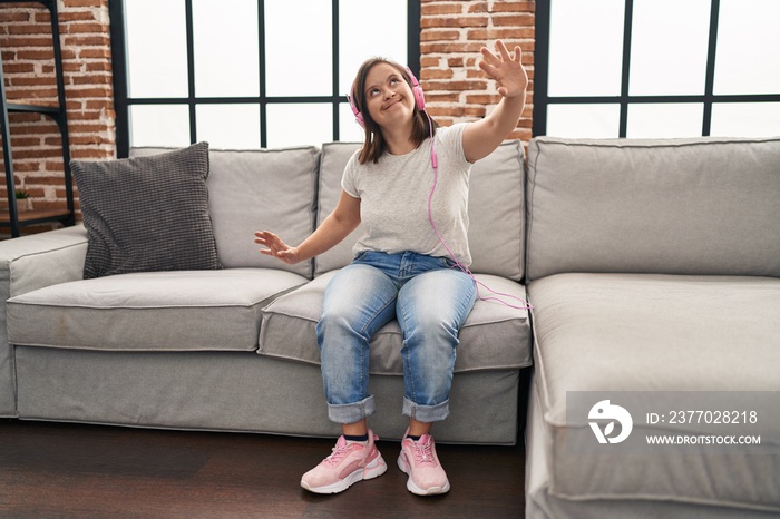 Down syndrome woman listening to music and dancing sitting on sofa at home