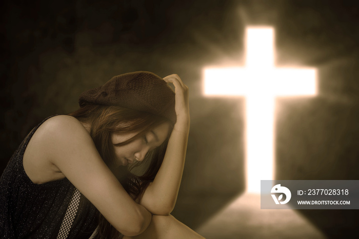 Sad woman sitting alone near a bright cross symbol