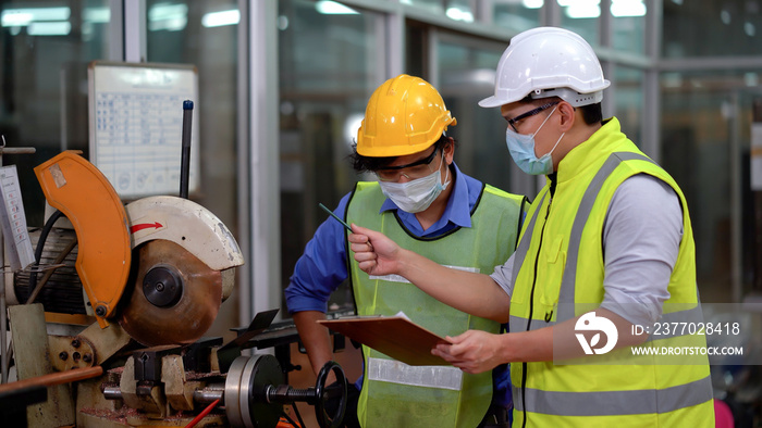 asian Engineer manager wearing protective face mask holding clipboard training mechanic worker operating machine industrial in industry manufacturing factory . during Coronavirus or Covid 19 pandemic