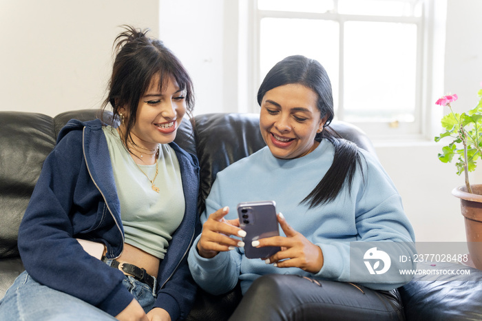 Two women sitting on sofa and looking at smartphone