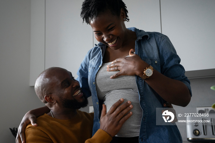 Smiling man touching pregnant woman’s belly in kitchen