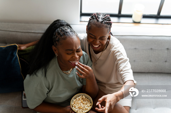 Lesbian couple eating popcorn while sitting on sofa at home