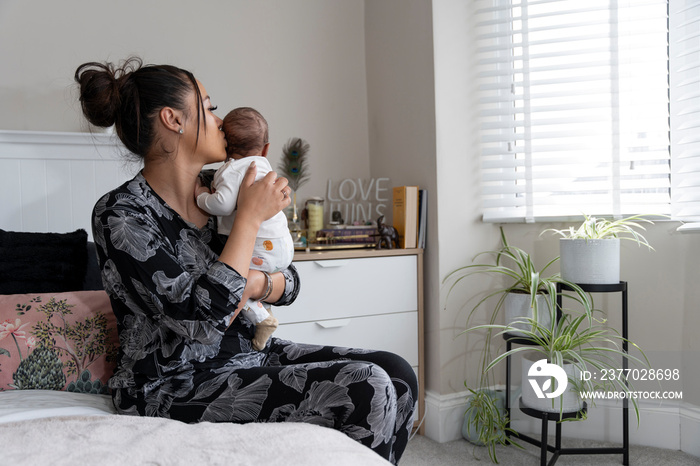 Mother carrying newborn baby girl while sitting on bed at home