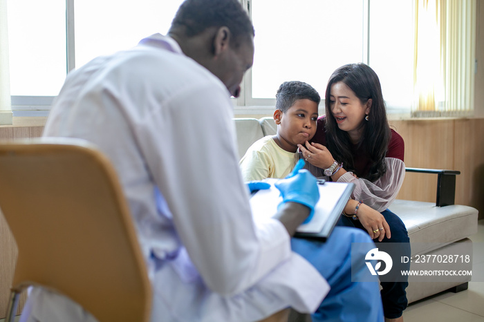 African pediatrician taking the patient’s history and examining child boy patient with his mother.