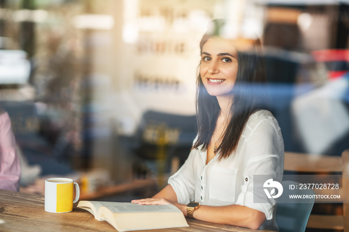 Young woman reading book in cafe behind the window