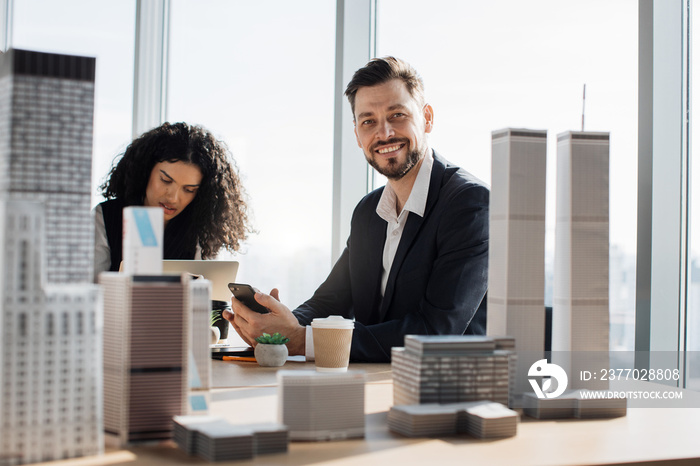 Diverse multi ethnic team of executive directors with young bearded male boss, on a meeting in conference room, sharing opinions, working with papers, laptop 3d city model