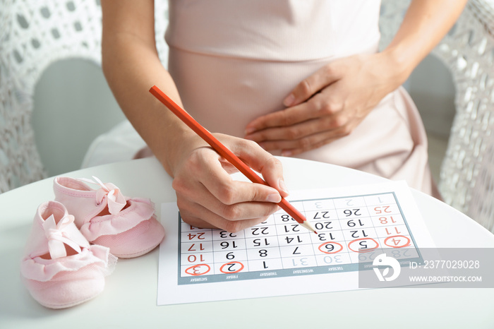 Pregnant woman with calendar sitting at table, closeup