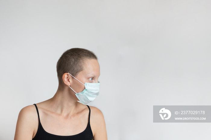 Profile side view of short haired young adult woman wearing protective facial mask on face against wall indoors. Coronavirus outbreak prevention. Vulnerable category person. Virus pandemic awareness