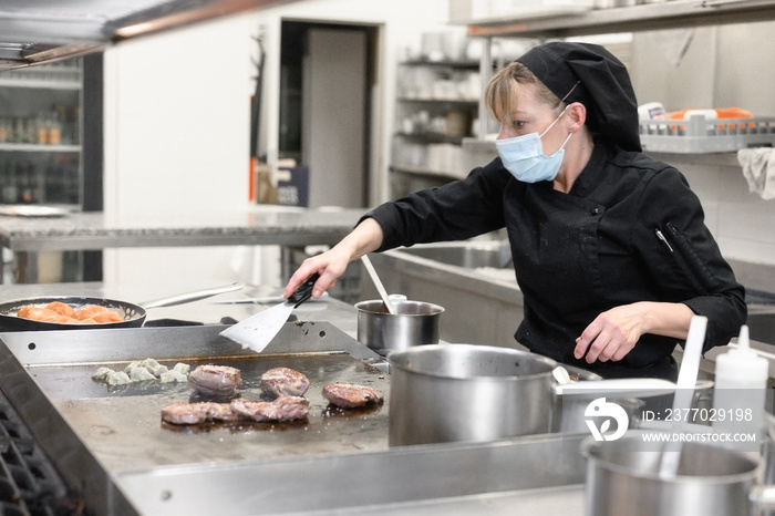 Woman Chef in protective face mask prepare food in the kitchen of a restaurant or hotel. Coronavirus prevention concept. High quality photo