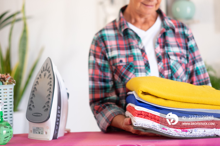 Closeup of mature woman in checkered shirt ironing clothes at home on ironing board