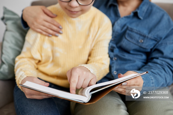 Close up of young girl with Down syndrome reading book with loving mother at home