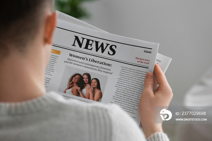 Young man reading newspaper at home, closeup