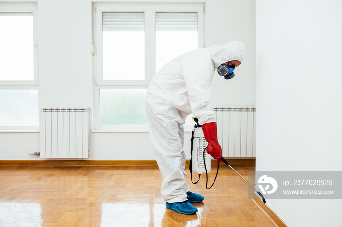 Exterminator in work wear spraying pesticide or insecticide with sprayer