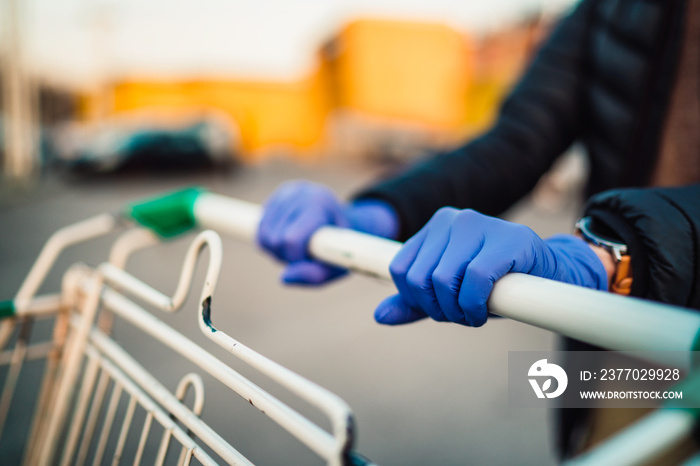 Close-up view of hands in rubber gloves pushing shopping carts.