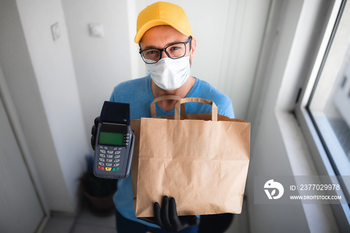 Delivery guy with protective mask holding box / bag with groceries and POS for contactless payment.