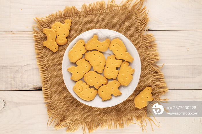 Several zoological cookies with a ceramic saucer and a jute napkin on a wooden table, macro, top view.