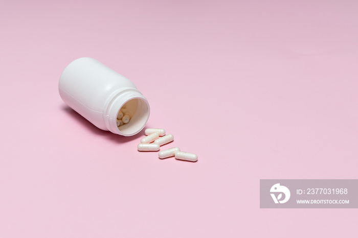 White medical capsules in white plastic bottle on light pink background with copy space for your text. Probiotics capsules. Template medical blog social media.