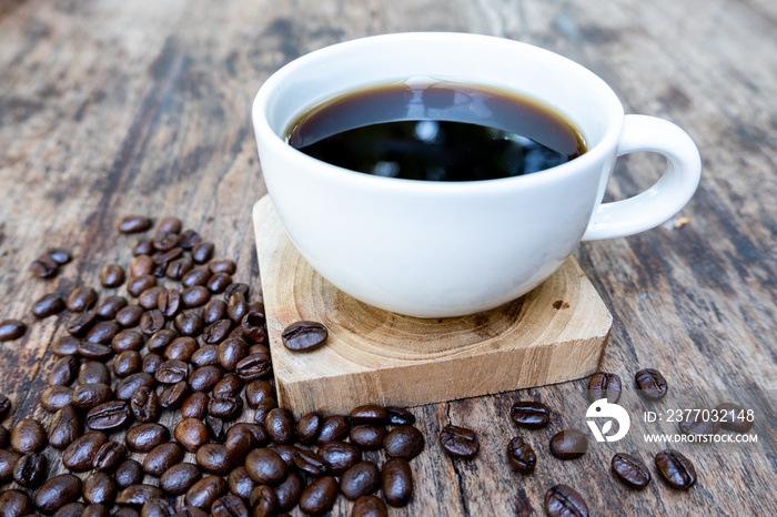 full of coffee beans spilling out bag on brown wooden background with a cup of black coffee