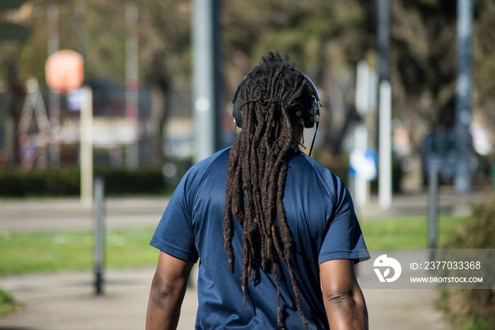 portrait on back view of african man with dreadlocks  walking in the street and listening music with headphones on head