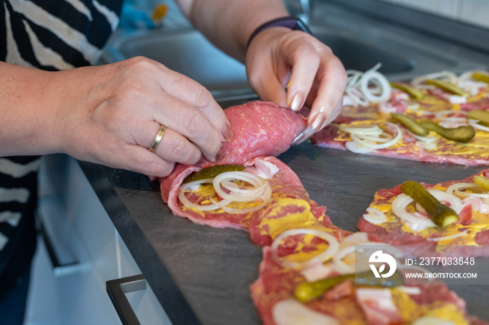 preparing beef rouladen, fresh raw meat coated with mustard and onions