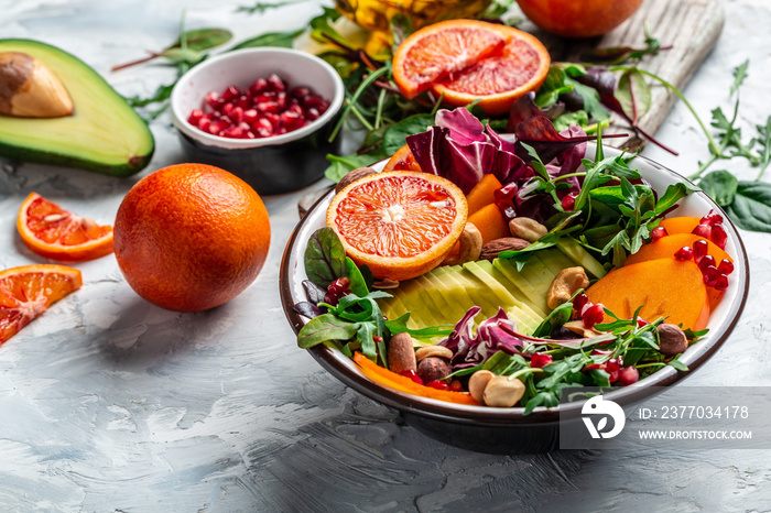 Healthy vegetarian buddha bowl salad with avocado, persimmon, blood orange, nuts, spinach, arugula and pomegranate on a light background, Long banner format, top view