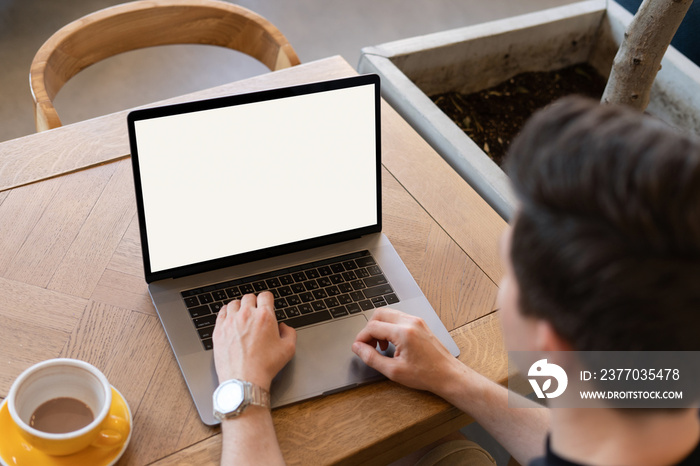 Top view of a man working at a computer sitting in a cafe with a cup of coffee. The concept of remote work, freelance