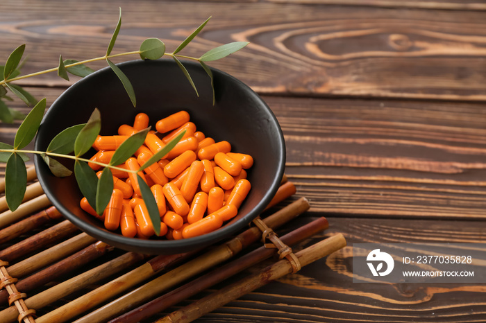 Bowl with turmeric powder capsules on wooden background, closeup