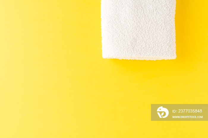 Overhead shot of clean bath towel on yellow table with copyspace