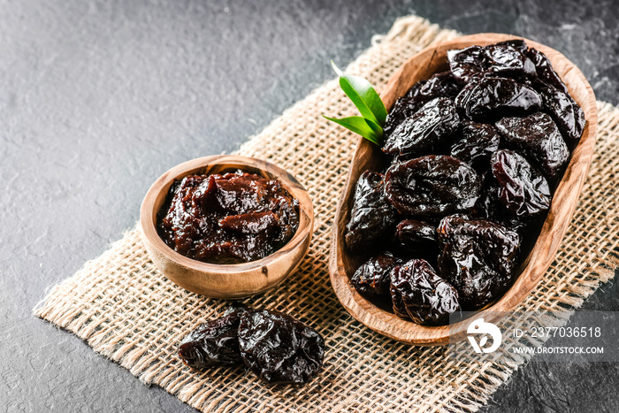 Fresh prunes in wooden bowl. Prunes on stone dark table. Prunes healthy food. Dried plums and jam in bowl.