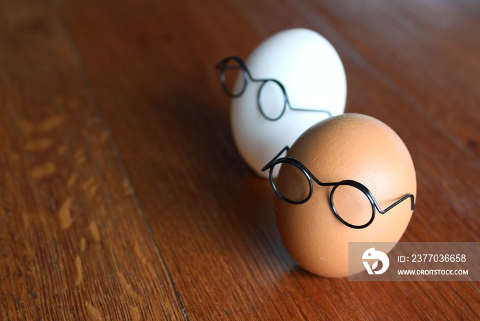 Similar but different concept. White egg and brown egg wear glasses on wooden table